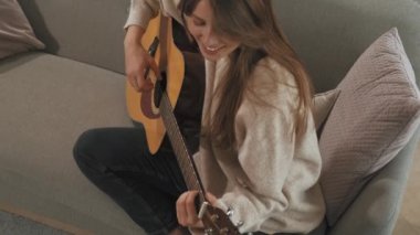 Top view video of young woman playing at acoustic guitar sitting in sofa.