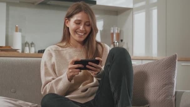 Footage Young Happy Woman Sitting Sofa Playing Games Smartphone — Stock Video