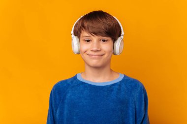 Kameraya gülümseyen genç çocuk kulaklık takıyor ve müzik meraklısı sarı arka plandan hoşlanıyor..