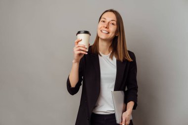 Bir kadın, laptopta çalışmaya ara verip bir fincan kahve içmeye bayılıyor. Stüdyo çekimi gri arkaplan üzerinde.