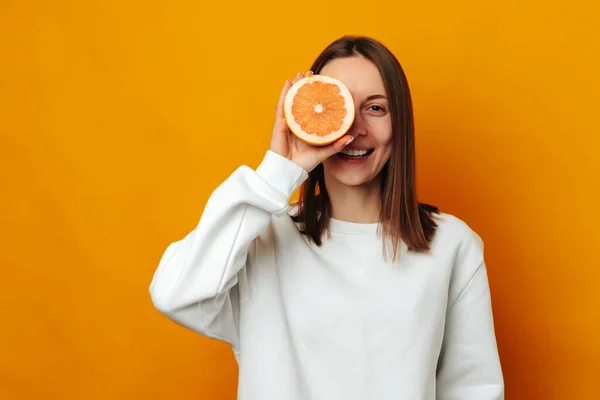 stock image Young woman suggests to take care of your face skin while holding a grapefruit. Studio portrait over yellow background.