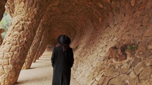 巴塞罗那Guel公园一名戴着黑色帽子和外套的年轻女子走路的镜头 — 图库视频影像