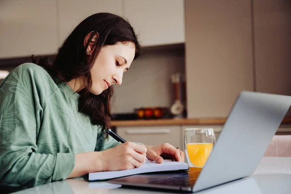 Yoğunlaşmış Genç Bir Kadın Mutfaktaki Laptopuyla Çalışıp Öğrenmeye Çalışıyor — Stok fotoğraf