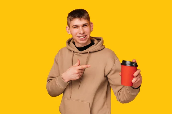 Молодий Усміхнений Чоловік Вказує Червону Каву Жовтому Фоні Студії — стокове фото