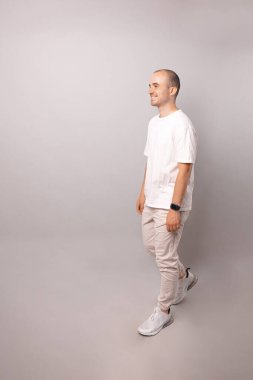 Kel, gülümseyen bir adamın gri arka planda yürüdüğü dikey bir vücut resmi..