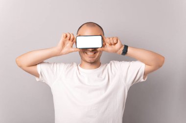 Geniş tebessüm eden kel adam gözlerini beyaz boş bir telefon ekranıyla kapatıyor..