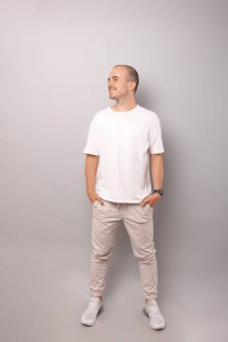 Kel bir adamın bütün vücudunun görüntüsü. Gri arka planda elleri ceplerinde duran bir adam..