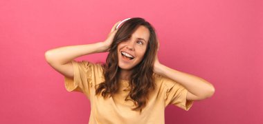 Kulaklık takan ve pembe arka planda eğlenen genç bir kadının afiş boyunda fotoğrafı..