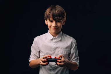 Beyaz tişörtlü genç bir çocuk siyah arka planda bir joystick ile oynuyor..
