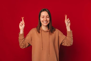 Genç kadın, koyu kırmızı arka planda parmaklarını çapraz yapıp gözlerini kapadı..