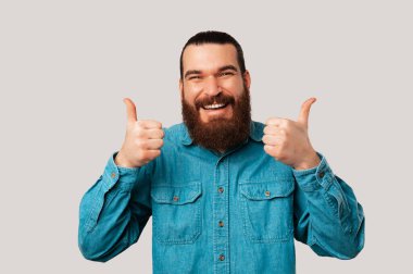 Kameraya gülümseyen bir gencin stüdyo portresi açık gri arkaplanda iki parmağını tutuyor..