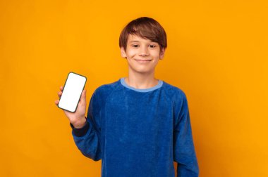 Neşeli genç çocuk elinde bir telefon tutuyor. Beyaz ekranlı, sarı arkaplan üzerinde kopya alanı olan bir telefon..