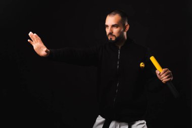 Genç ve ciddi bir adam siyah arka planda bir nunchaku dövüş sanatını icra ediyor..