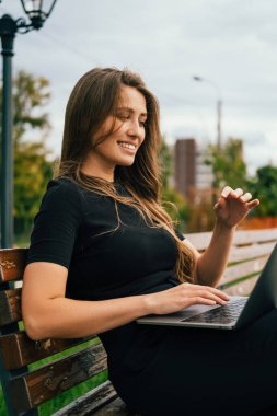 Rüzgarlı bir günde bankta oturmuş laptopuyla çalışan bir kadının dikey çekimi..