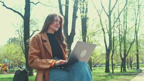 若い陽気な女性が市内で屋外に座っている間 ラップトップでオンライン会議を持っています — ストック動画