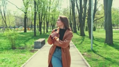 Genç, çekici ve gülümseyen bir kadının parkta yürüdüğü ve uçan saçlarıyla etrafında döndüğü bir video..