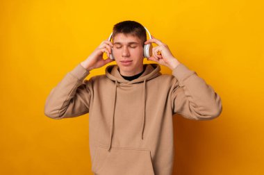 Yakışıklı genç adam sarı arka planda kulaklık takarken kapalı gözlerle müzik dinlemekten hoşlanır..