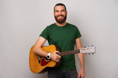 Gülümseyen yakışıklı sakallı adam akustik gitar tutarken öğretmeye hazır..