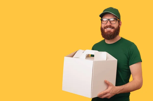 Studio shot of a handsome delivery man holding a white delivery cake box over yellow background.