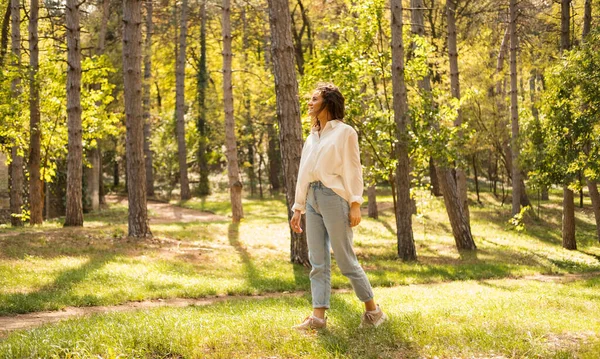 若い穏やかな女性が晴れた日に風と自由を楽しんで森の木々の間を歩いています — ストック写真