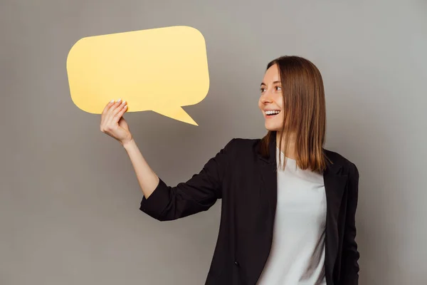 stock image Ecstatic young woman wearing jacket is holding a yellow bubble speech beside her.