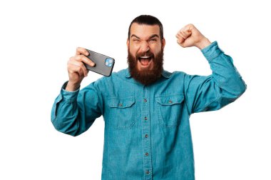 Mest olmuş genç sakallı adam telefonunu tutarken kazanan hareketi yapıyor..