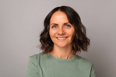 Kameraya gülümseyen orta yaşlı bir kadının gri arka plandaki portresini kapat..