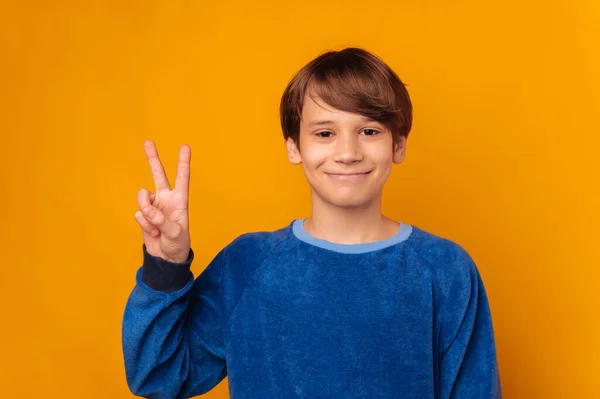 Χαμογελώντας Έφηβος Αγόρι Φορώντας Μπλε Δείχνει Χειρονομία Νίκης Πάνω Κίτρινο — Φωτογραφία Αρχείου