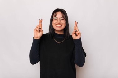 Gülümseyen kadın parmakları çapraz ve gözleri kapalı beyaz arka plan üzerinde bir dilek tutar.