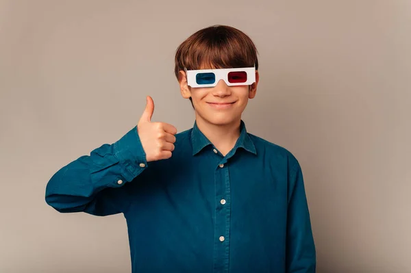 Handsome little teen boy wearing 3D glasses recommends you to see this movie.  Studio portrait over grey background.