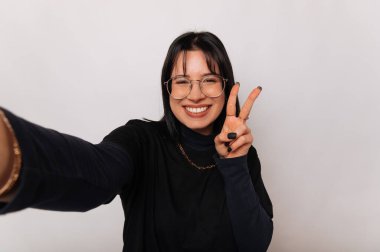 Heyecanlı kadın bir stüdyoda beyaz arka planda Ziyaretçi jesti gösterirken selfie çekiyor..