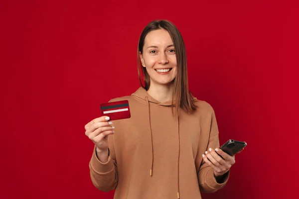 Neşeli Kadın Telefonunu Kartını Kırmızı Arka Planda Tutarken Mobil Bankacılık — Stok fotoğraf