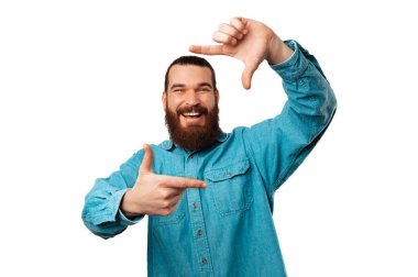 Neşeli sakallı adam elinde tuttuğu parmak çerçevelerine bakıyor. Stüdyo çekimi beyaz arkaplan üzerinde.