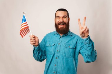 Mutlu genç sakallı adam beyaz arka planda Ziyaretçi jesti ve ABD bayrağını tutuyor..