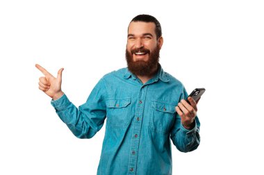 Neşeli genç adam telefonunu tutarken fotokopi alanını işaret ediyor. Beyaz arkaplan üzerinde stüdyo resmi.