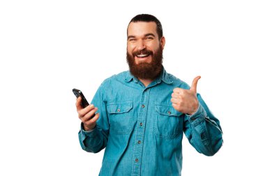 Mest olmuş sakallı bir adam elinde telefonuyla bu teklif için baş parmağını kaldırıyor. Stüdyo çekimi beyaz arkaplan üzerinde.