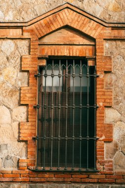 Beyaz taş ve tuğladan yapılmış bir duvarda metal parmaklıklarla kaplı güzel bir pencerenin dikey görüntüsü..