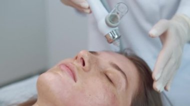 Kozmetikçinin ürün serumuyla cilde nüfuz eden yaşlanmayı önleyici kozmetik cihaz prosedürünü kullandığı görüntüler.