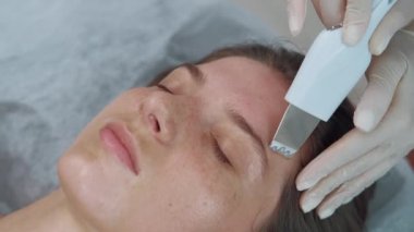 Güzellik salonunda yüz temizleme için ultrasonik cihaz kullanan kozmetikçinin videosu..