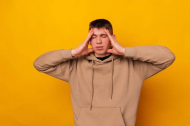 Sarı arka planda duran ve başı ağrıyan genç adamın fotoğrafı..