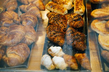 Some fresh sweet pastries and croissants with chocolate displayed in the window of a cafe. clipart