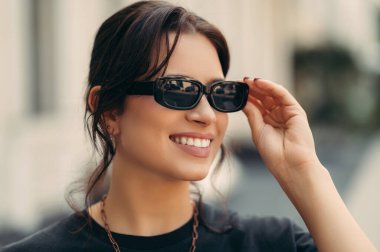 Açık havada, güneş gözlüğünü takan gülümseyen genç bir kadının yaz portresini kapatın..