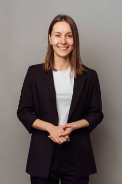 Gri bir stüdyoda ceketli, kendine güvenen güzel bir kadının dikey çekimi..