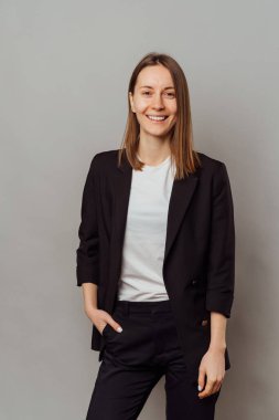 Gri arka planda siyah ceket giyen, rahatlamış, rahatlamış bir kadının dikey çekimi..