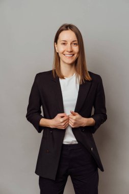 Ceket giyen kendine güvenen bir kadının dikey görüntüsü gri arka planda kameraya gülümsüyor..