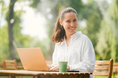 Yakışıklı genç bayan, dışarıda, bir kafede dizüstü bilgisayarıyla çalışmaktan hoşlanıyor..