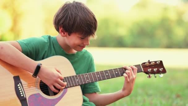 公園の少年がアコースティックギターを練習して演奏する様子 — ストック動画