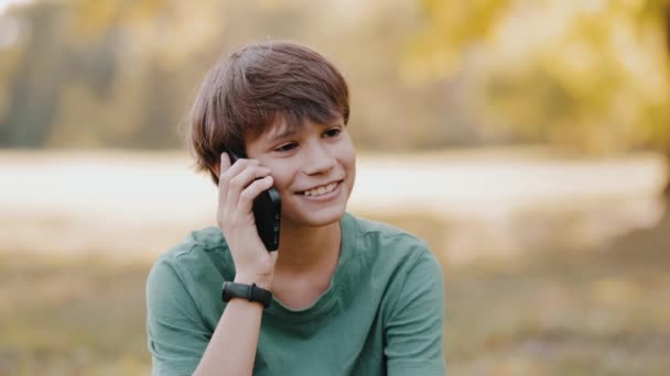 Νεαρό Αγόρι Κάθεται Στο Πάρκο Και Μιλάει Στο Smartphone Και — Αρχείο Βίντεο