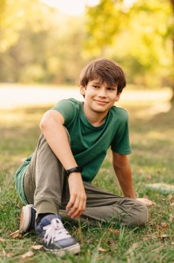 Okuldan sonra çimde oturan ve rahatlayan genç bir çocuğun dikey fotoğrafı..