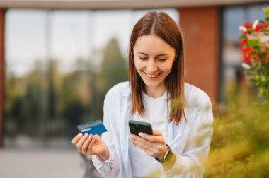 Neşeli genç bir kadın internetten kredi kartıyla ya da kredi kartıyla bir şeyler alıyor..